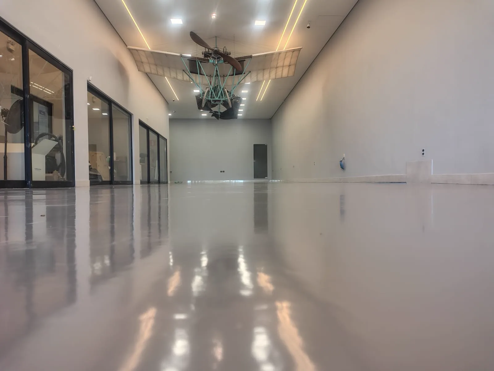 Salão comercial com piso em resina epóxi autonivelante aplicado pela MG, acabamento cinza espelhado refletindo as luminárias