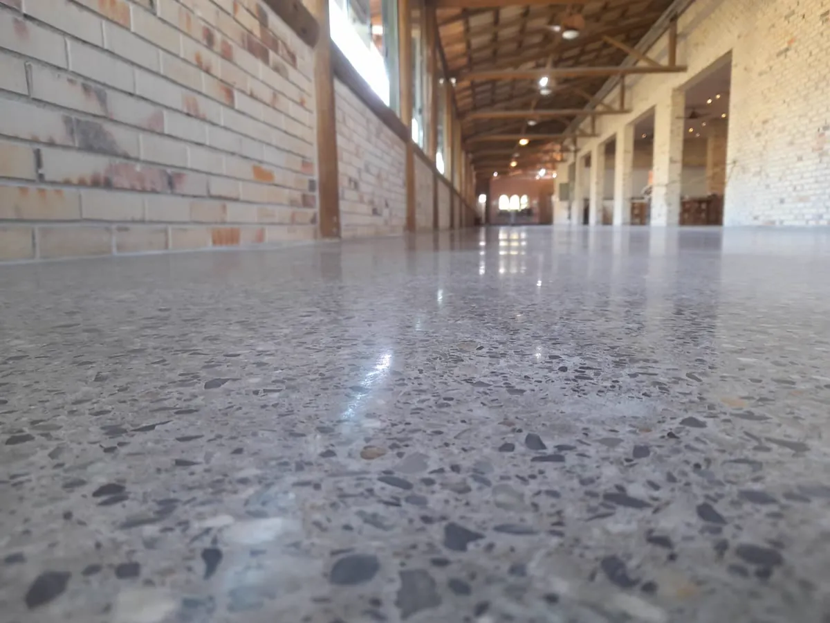 Galpão com piso de concreto polido pela MG, agregado aparente e reflexo espelhado ao longo do corredor